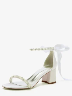 Chaussures de mariée blanches à talons carrés ornées de perles et de strass avec bride à la cheville.
