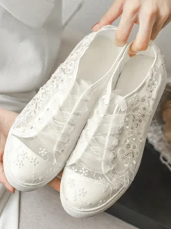 Chaussures de mariée plates ivoire à bout rond ornées de perles et lacées style baskets décontractées.
