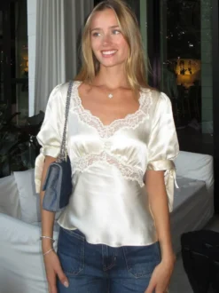 Chemisier en satin à col V bouffant et manches courtes bouffantes orné de dentelle avec ceinture à nouer dans le dos et coupe ajustée. Élégante chemise pour femme.