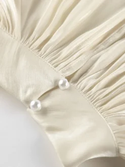 Chemisier oversize en satin crème brillant à col montant froncé manches ballon et poignets perlés