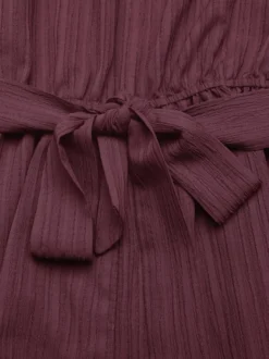 Combinaison-short d'été décontractée pour femme mauve asymétrique avec ceinture et tissu texturé à nouer à la taille.
